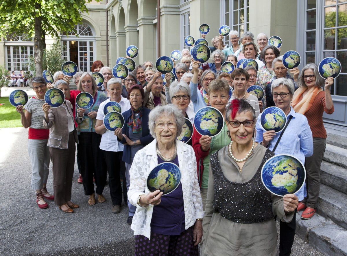 Περίπου 40 μέλη των Klimaseniorinnen κρατούν μικρές χάρτινες υδρόγειες σφαίρες
